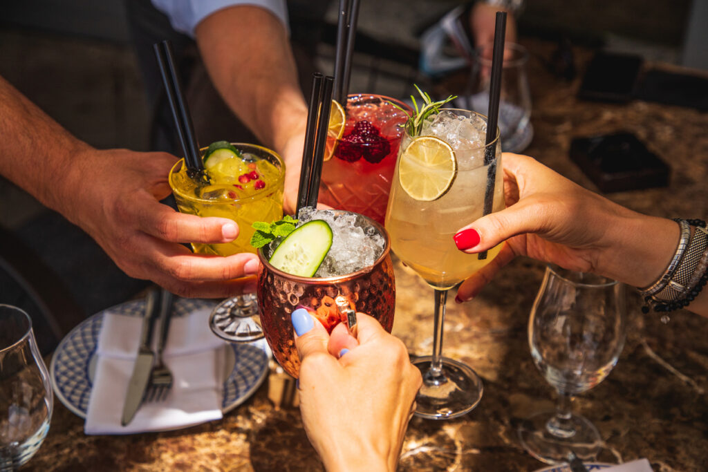 4 Freunde greifen nach Ihrem Glas bei einem Cocktail Tasting in Berlin.