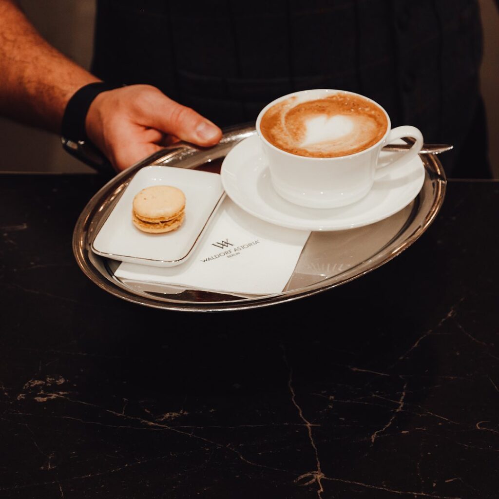 Tasse Cappuccino mit Macaron auf Tablett.