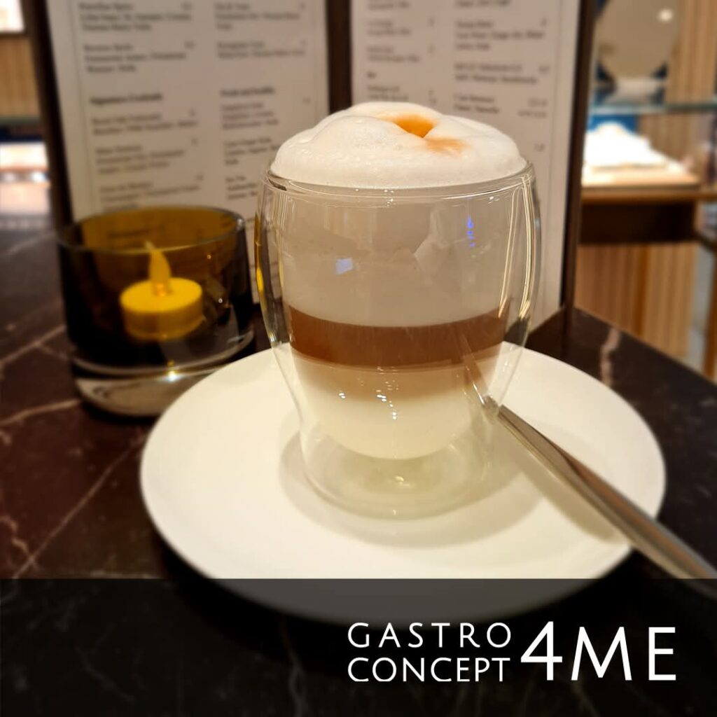 Cappuccino im Glas mit Sahnehaube auf Teller